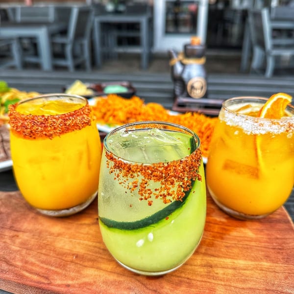 Three vibrant cocktails, two orange and one green with cucumber, on a wooden board at Chronic Sushi.